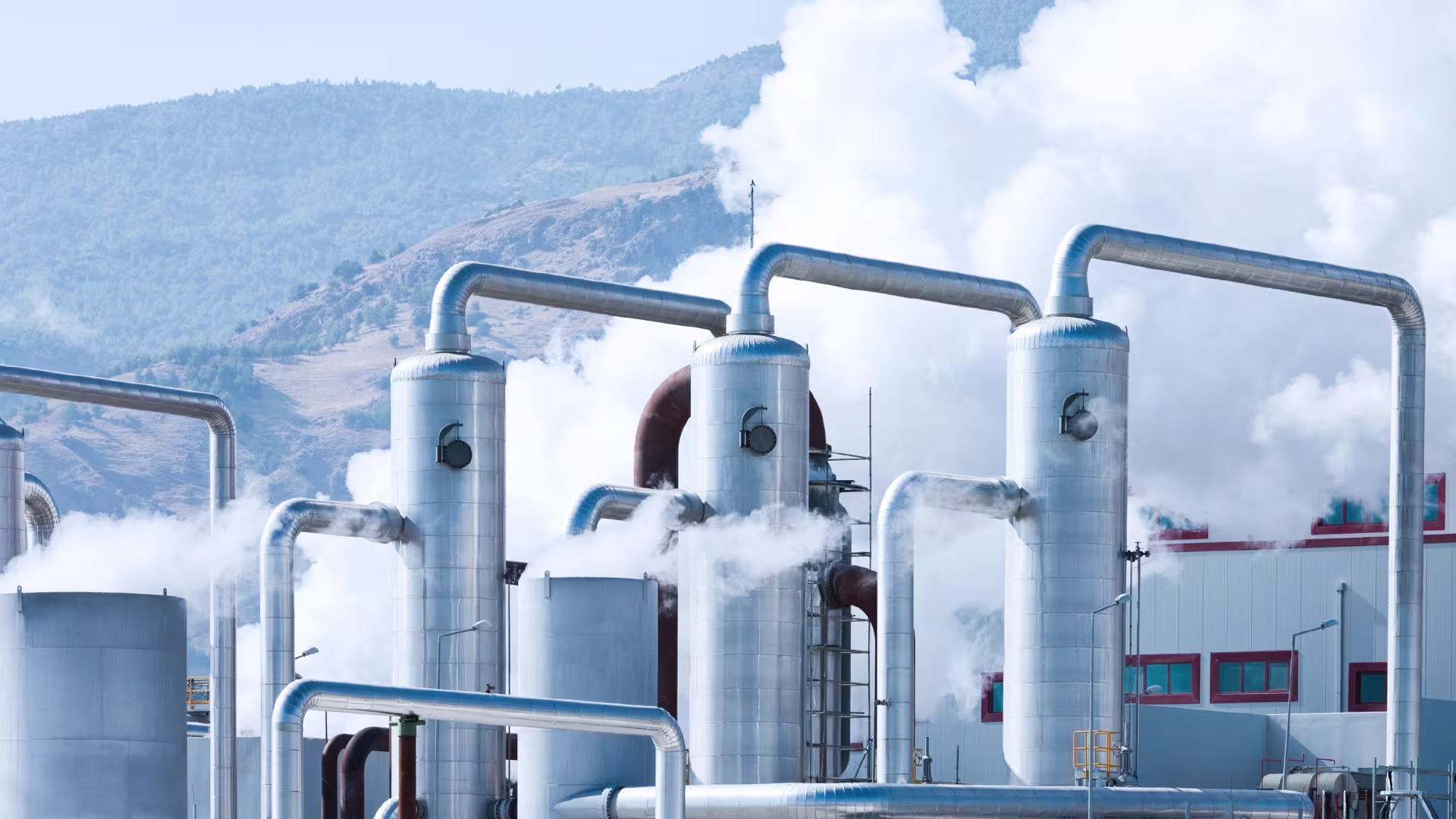 Industrial facility with steam pipes in front of a mountain landscape.