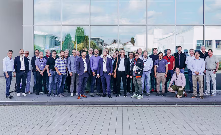 Gruppenfoto einer großen Teilnehmergruppe vor einem modernen Gebäude mit Glasfassade.