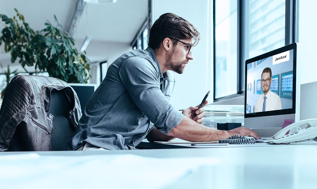 Junger Mann arbeitet konzentriert an einem Schreibtisch mit einem Laptop, auf dem eine Videokonferenz läuft